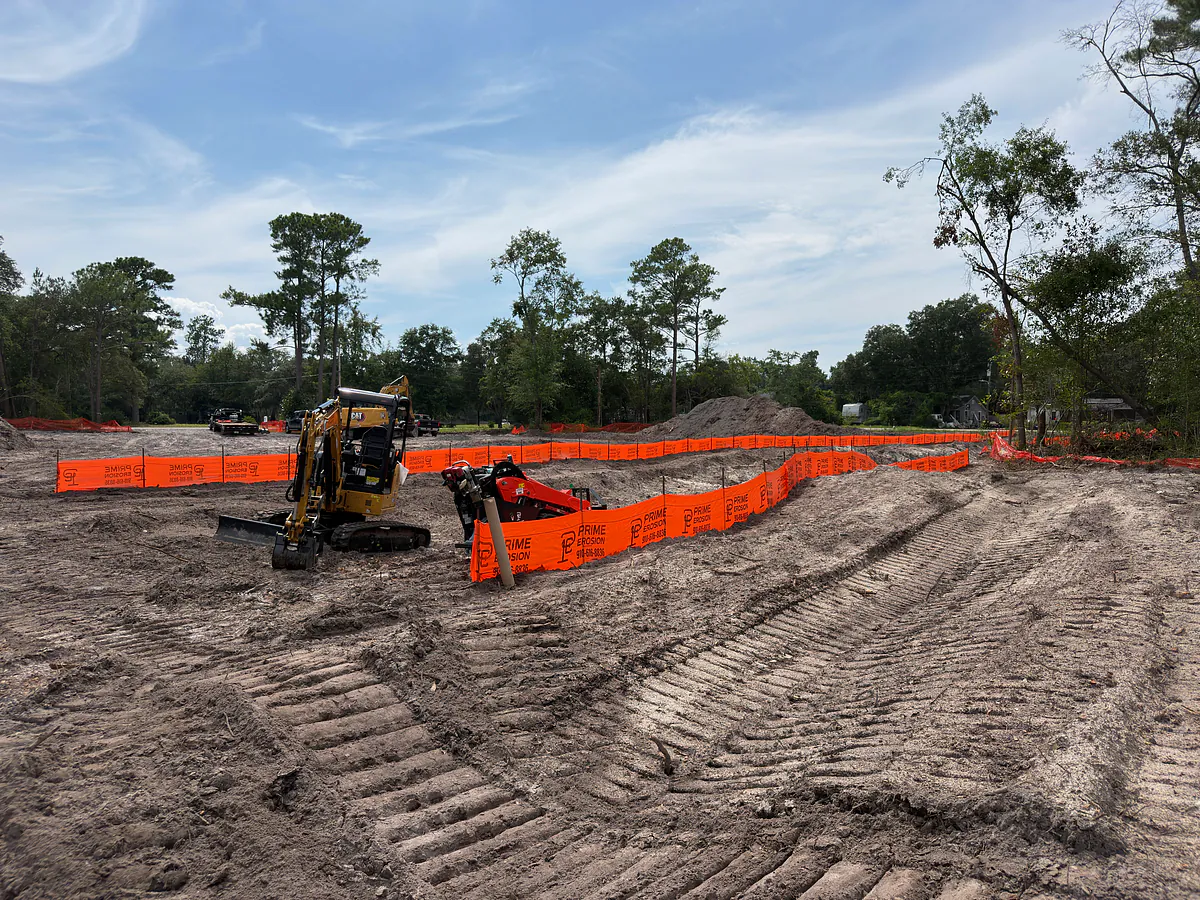 Mini excavator trenching silt fence around a cleared commercial pad in wilmington nc